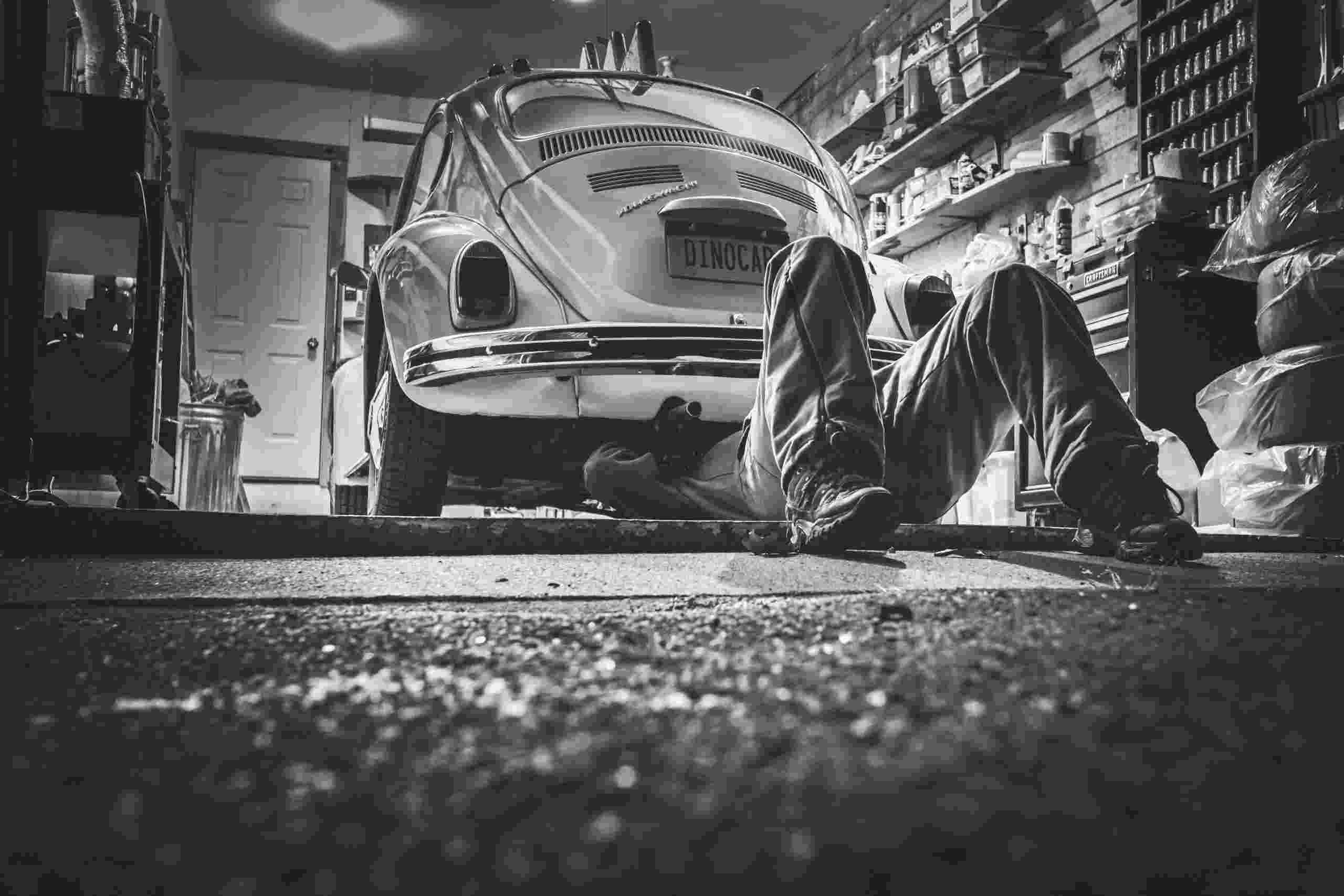 Automotive technician working beneath a classic vehicle inside a repair garage, representing Fleet vehicle repair financing, automotive lift financing, loans for purchasing a repair facility, EV technician training financing, and paint booth financing for repair shops expanding equipment, facilities, and technician capabilities.