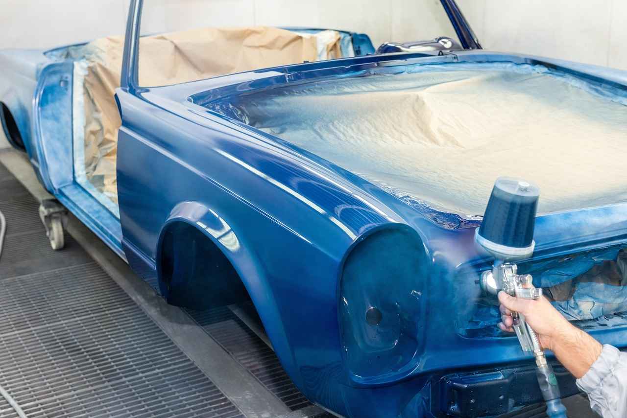 Technician applying blue paint to a classic vehicle inside a professional automotive paint booth, showcasing business growth opportunities through Automotive merger financing, auto repair working capital, repair facility growth capital, wheel balancer financing, and EV repair technology financing for collision centers, restoration shops, and modern automotive service facilities.