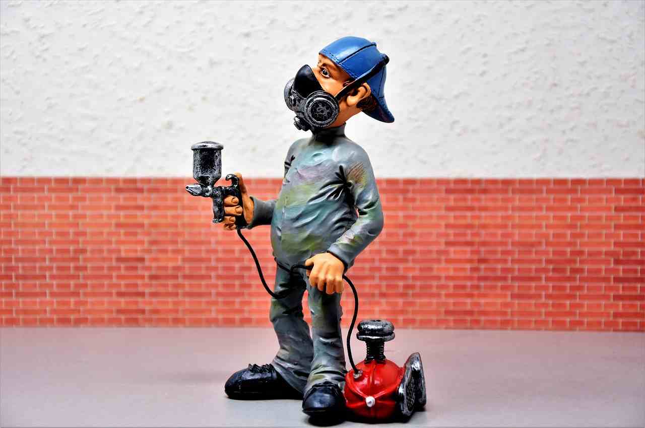 Automotive technician figurine holding a paint spray gun and wearing a respirator mask, symbolizing auto repair shop growth through Vehicle lift loans, repair shop buyout loans, repair shop technology financing, vehicle diagnostic system financing, and garage construction financing for modern automotive service businesses investing in equipment, technology, acquisitions, and facility expansion.