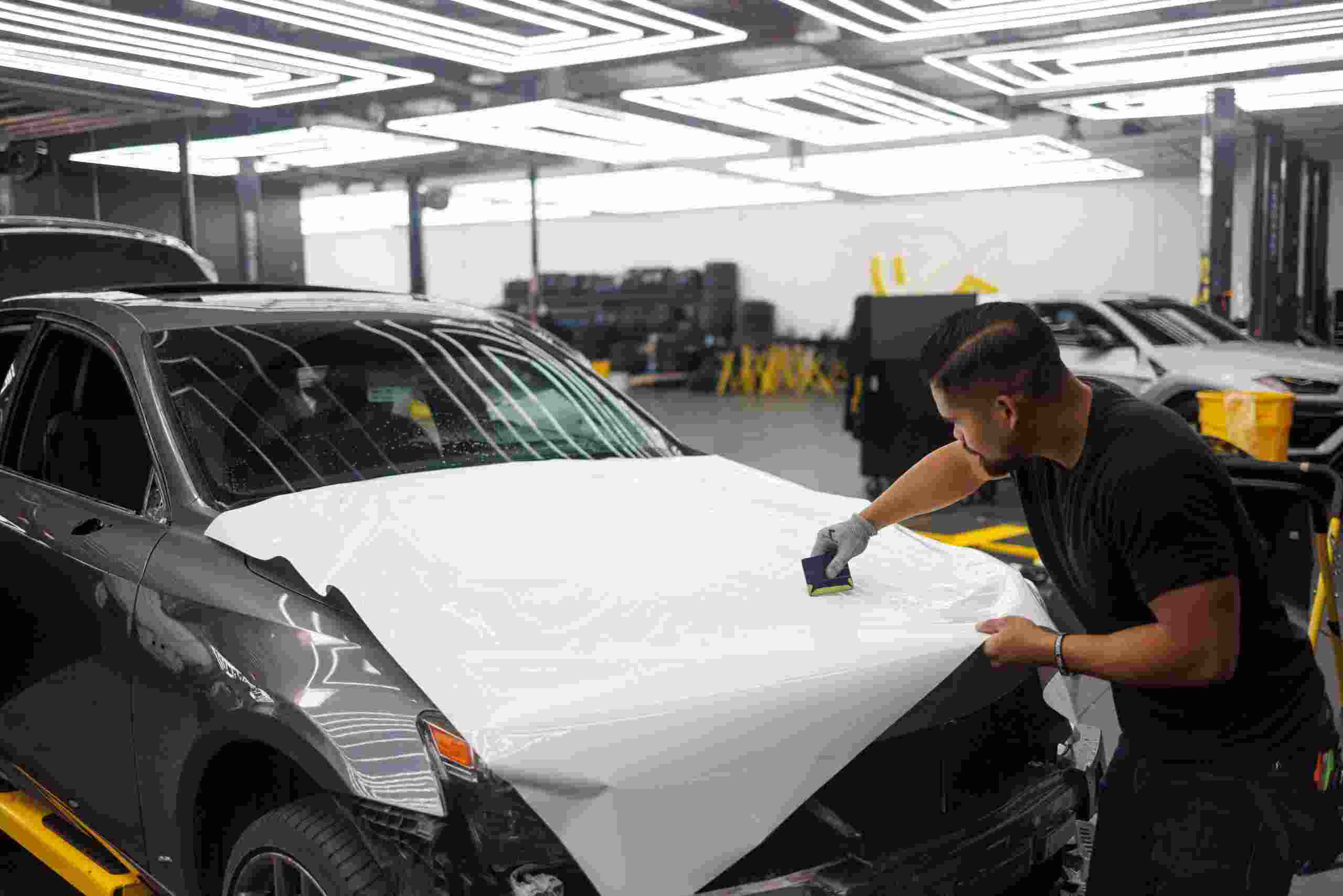 Automotive technician installing protective film on a vehicle inside a modern service facility, representing Collision shop funding, how to finance an auto repair shop, EV service center financing, dent repair equipment financing, and garage building loans used by automotive businesses to expand facilities, purchase equipment, and support long-term growth.