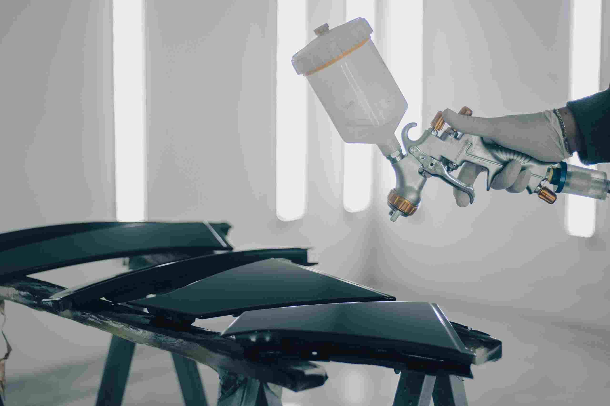 Automotive painter using a professional spray gun inside a modern paint booth while refinishing vehicle body panels, representing Garage equipment financing, fleet maintenance financing, body shop technology financing, repair facility purchase loans, and EV repair shop financing for automotive businesses investing in advanced equipment, facility growth, and specialized repair services.