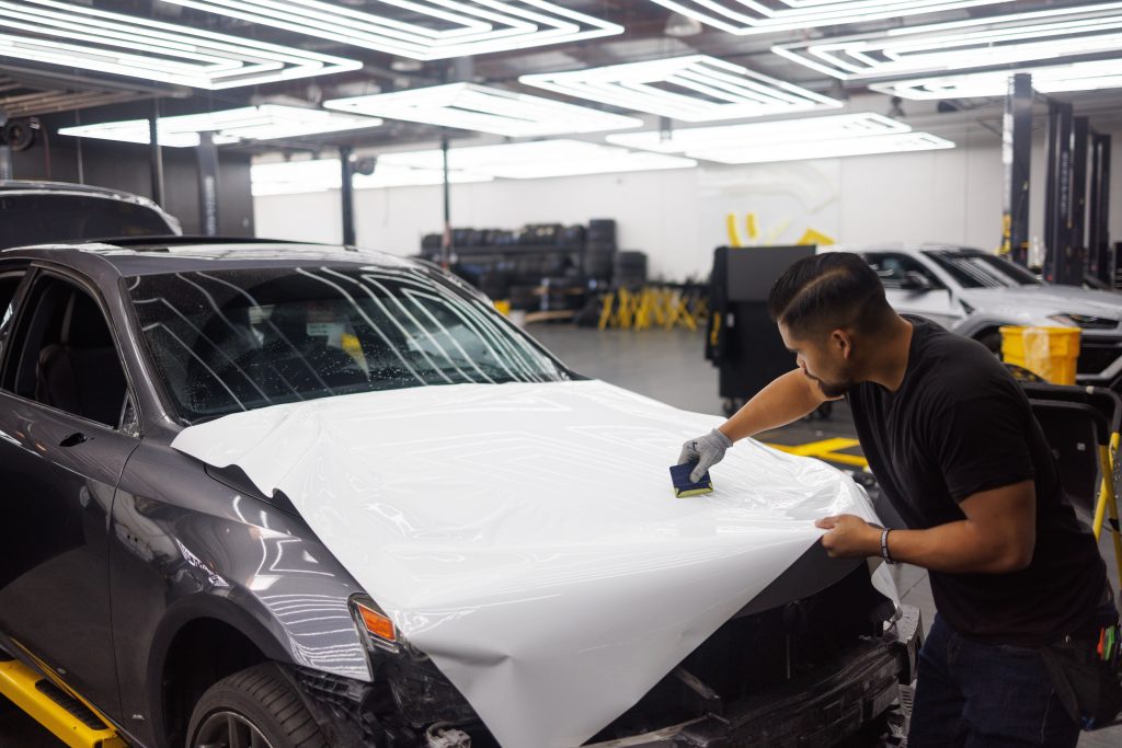 Automotive technician applying protective film to a vehicle inside a modern service facility, representing EV battery service equipment financing, automotive digital workflow financing, mechanic business financing options, and fleet maintenance financing for automotive businesses.