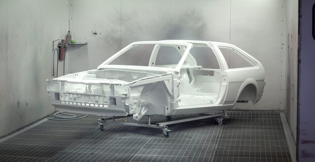 White automotive body shell positioned inside a professional paint booth, representing Automotive property acquisition loans, auto repair software financing, automotive revenue financing, and electric vehicle service equipment financing for automotive repair and collision businesses.