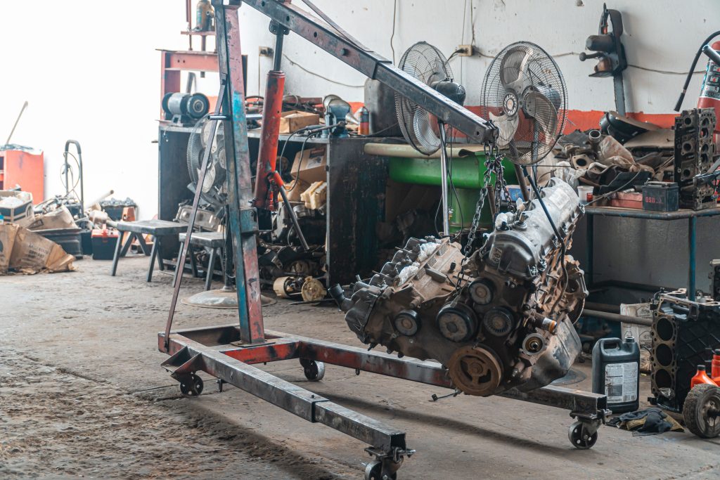 Automotive engine suspended from an engine hoist inside a repair shop representing Garage construction financing, additional repair location financing, repair shop payroll financing, repair shop technology upgrades, and an auto shop loan for automotive business growth.