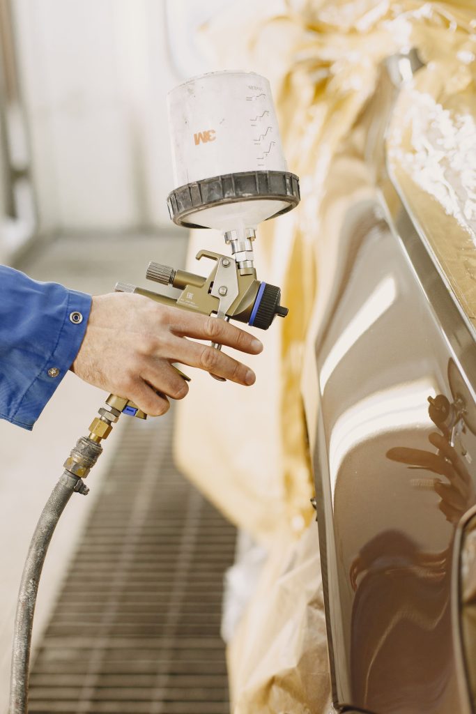 Automotive technician using a professional spray gun to refinish a vehicle body panel, representing Repair facility development financing, automotive cash flow financing, electric vehicle diagnostic financing, and EV battery service equipment financing for modern automotive repair businesses.
