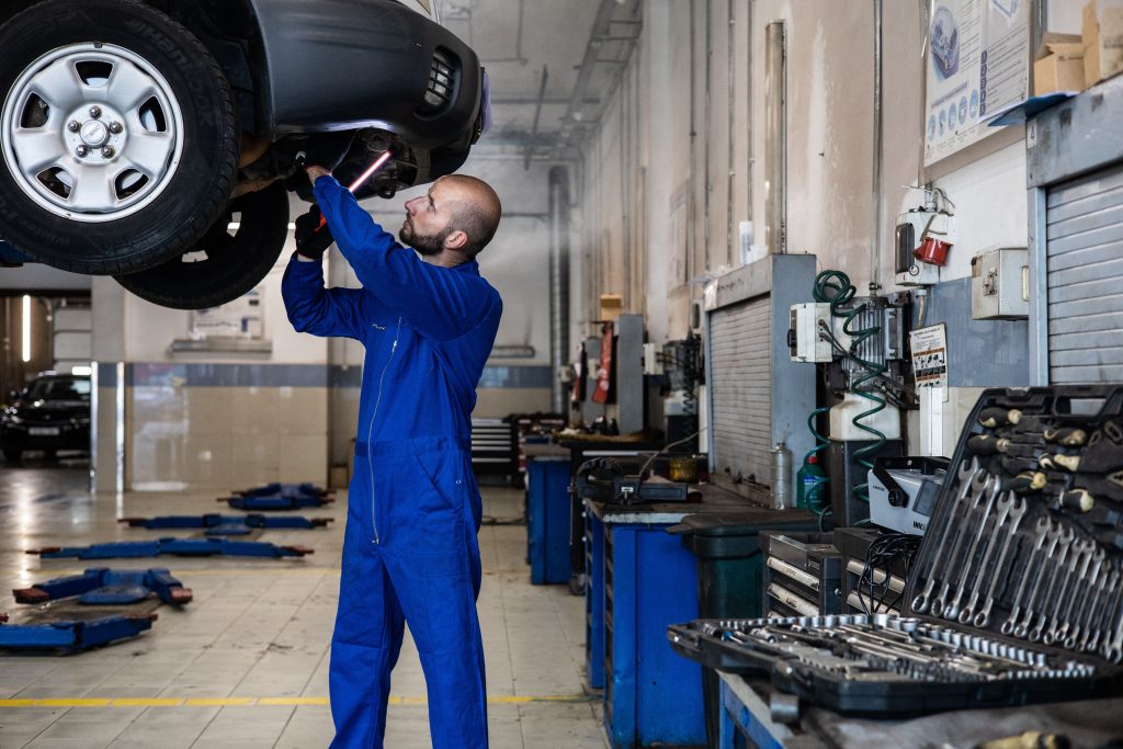 Mechanic working underneath a raised vehicle in an automotive repair facility representing Collision shop funding, auto repair shop expansion loans, wheel inventory financing, repair facility purchase loans, and mechanic business financing for automotive businesses.